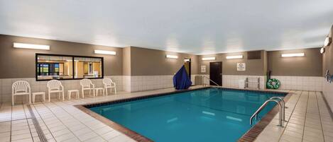 Une piscine intérieure à l’eau claire, entourée de chaises blanches et d’une serviette bleue.
