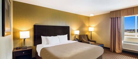 A hotel room with a large bed, two bedside lamps, a chair, a nightstand, and a window with curtains.