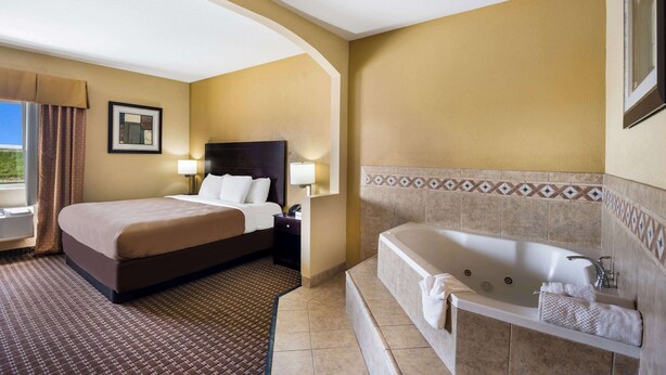 A hotel room with a large bed, a separate bathroom with a bathtub, and a window with curtains. - Quality Inn Des Moines North (Des Moines)