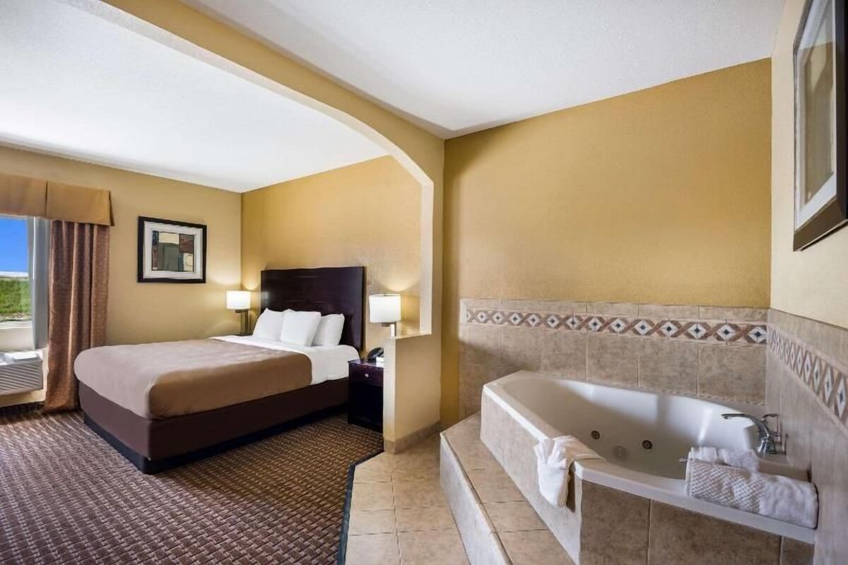 A hotel room with a bed, a bathroom with a bathtub, and a window with curtains.