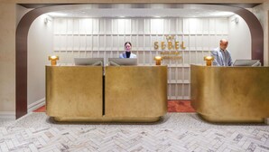 A reception area with two reception desks, a wall with the text 'The Sebel Melbourne,' and a herringbone-patterned floor. - The Sebel Melbourne Flinders Lane (Melbourne)