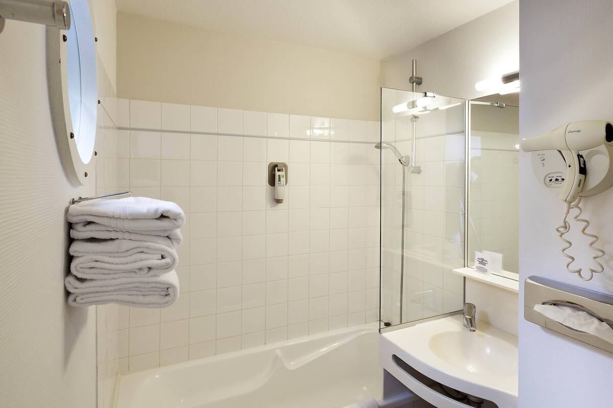 Une salle de bain moderne avec une douche à parois de verre, une baignoire blanche, un lavabo et un porte-serviettes avec des serviettes pliées.