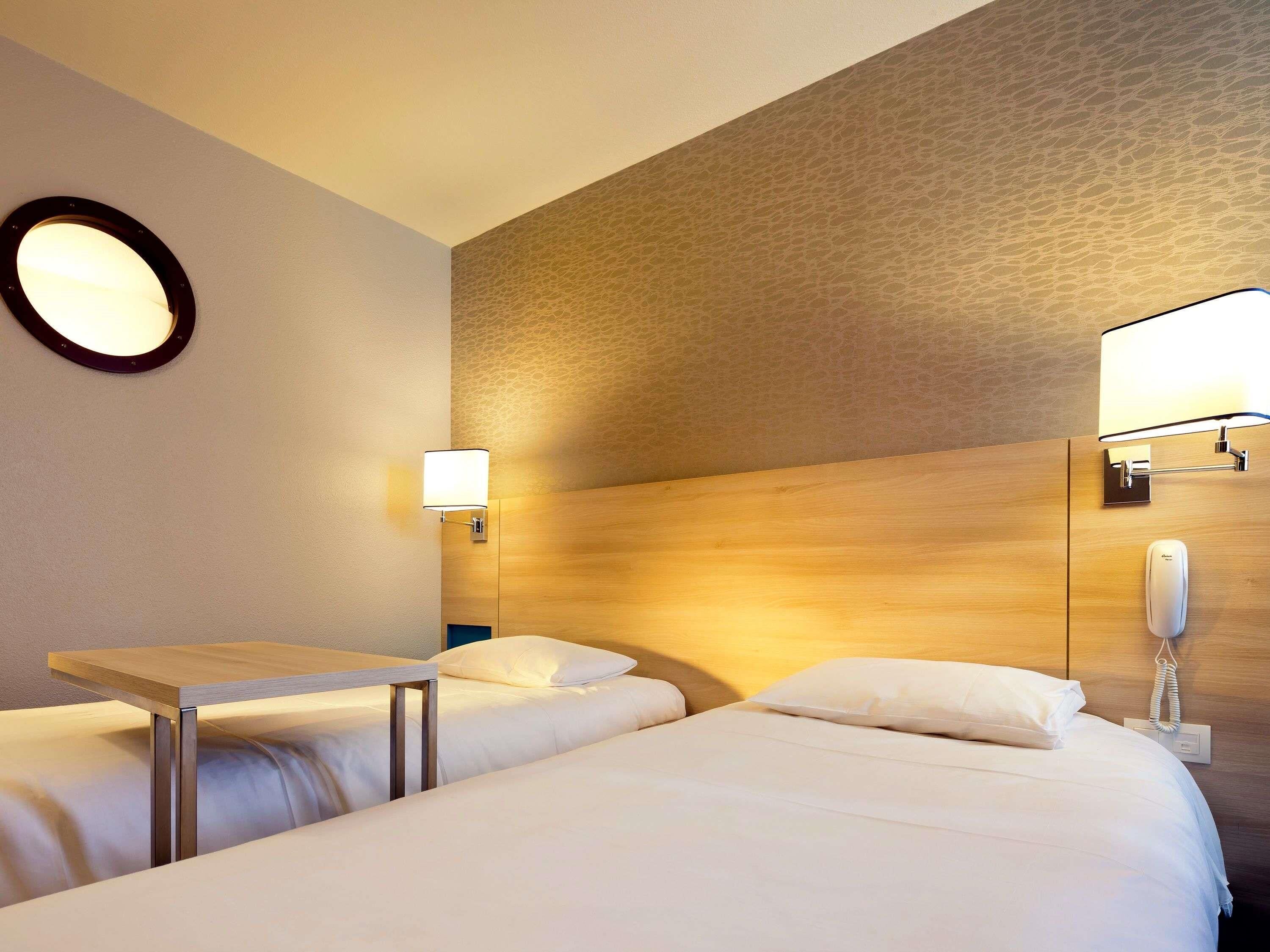 Een hotelkamer met twee bedden, een ronde spiegel aan de muur en een telefoon op het nachtkastje.