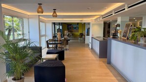 Een moderne hotellobby met een houten vloer, zwarte zachte zitplaatsen en een receptiebalie met een menubord.