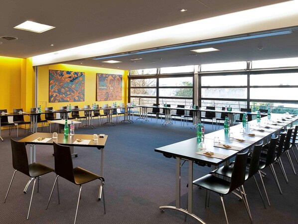A conference room with multiple tables and chairs, large windows, and artwork on the walls. - ibis Styles Ouistreham (Ouistreham)