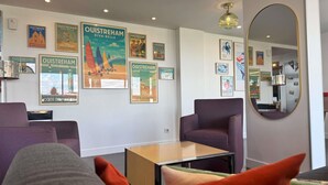 Een hotelkamer met een bank, fauteuil, klein tafeltje en een muur versierd met oude posters.