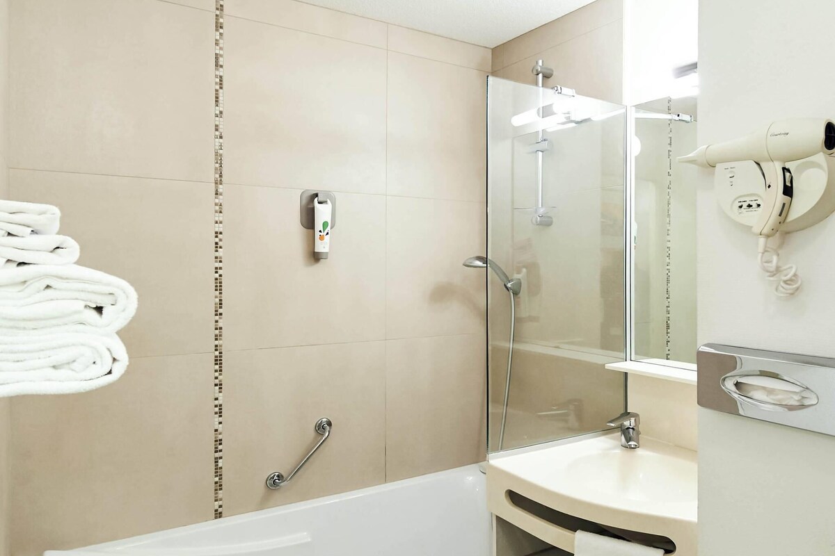 A modern bathroom with a glass-enclosed shower, a white bathtub, and a vanity with a mirror.