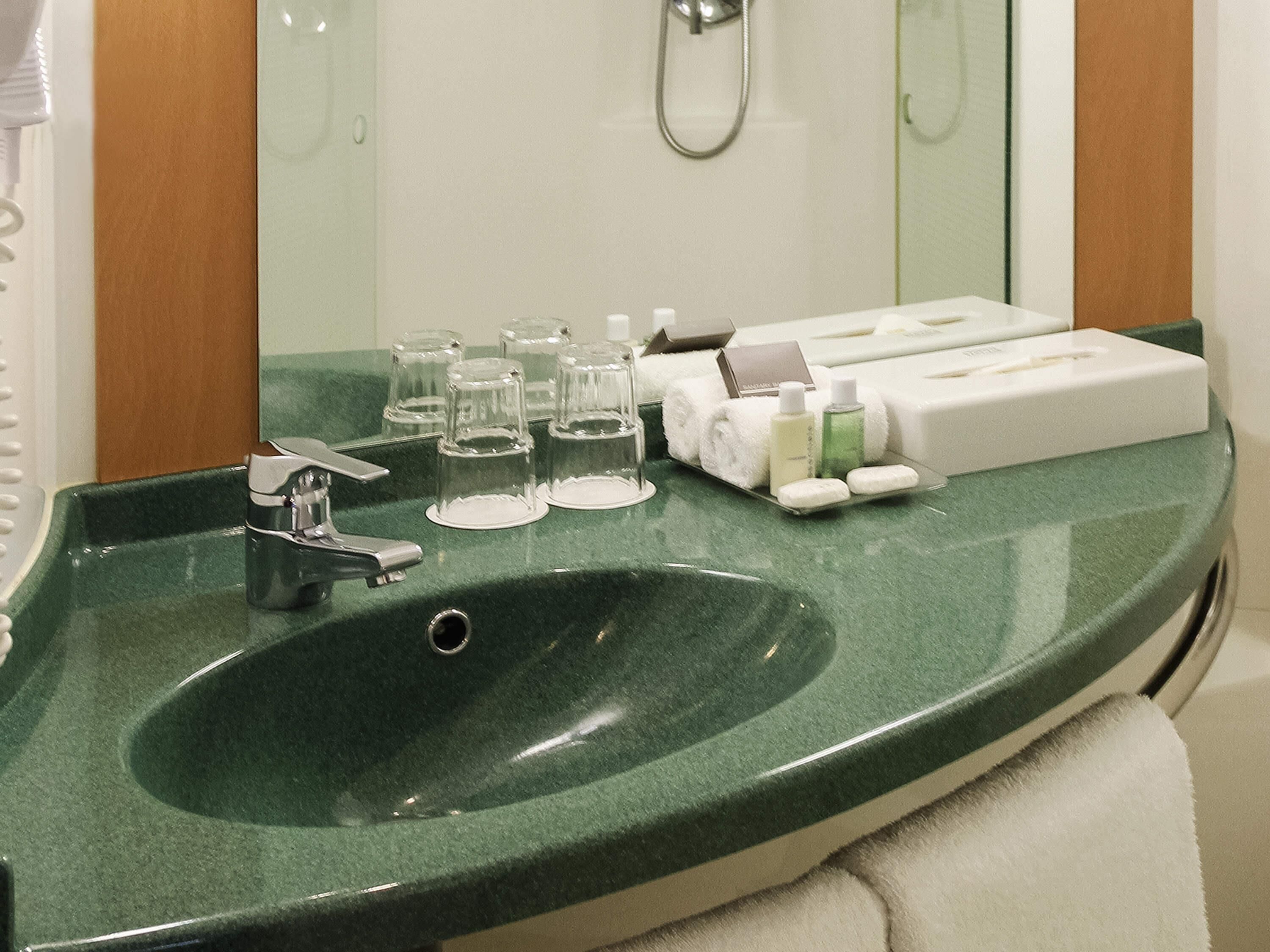 Une salle de bain avec un lavabo vert, un miroir, une douche et des articles de toilette posés sur le comptoir.