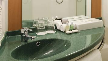 Une salle de bain avec un lavabo vert, un miroir, une douche et des articles de toilette posés sur le comptoir.