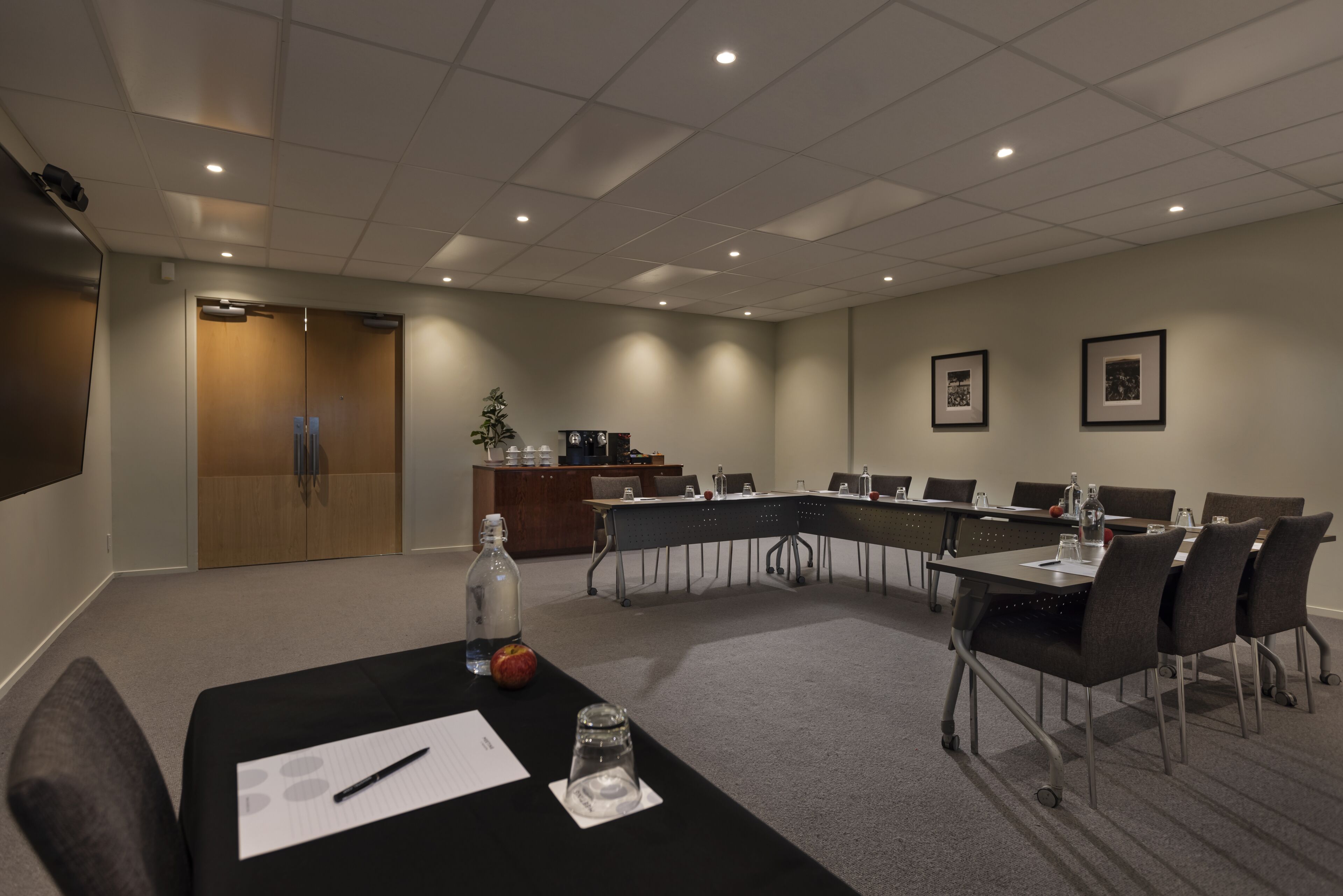 Un salón de conferencias con una larga mesa, sillas, un atril y una pantalla para proyector.