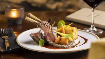 A plate of food with a lamb shank, vegetables, and sauce, accompanied by a glass of red wine and a candle.