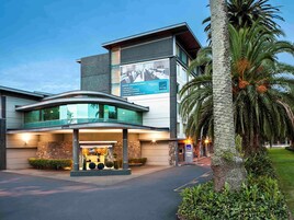 Un hotel moderno con entrada curva, fachada de piedra y un gran anuncio que ofrece salones para reuniones y estacionamiento.