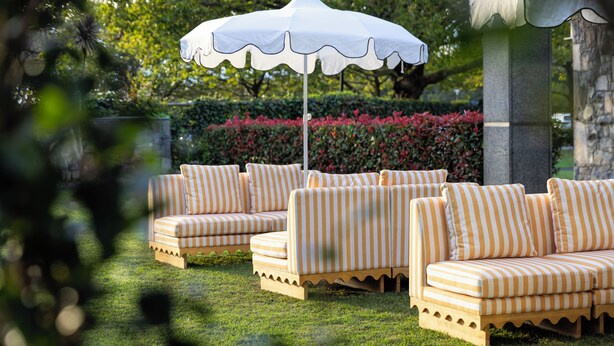 Outdoor seating with striped cushions, a white umbrella, and a stone pillar in a garden setting. - ibis Auckland Ellerslie (Auckland)