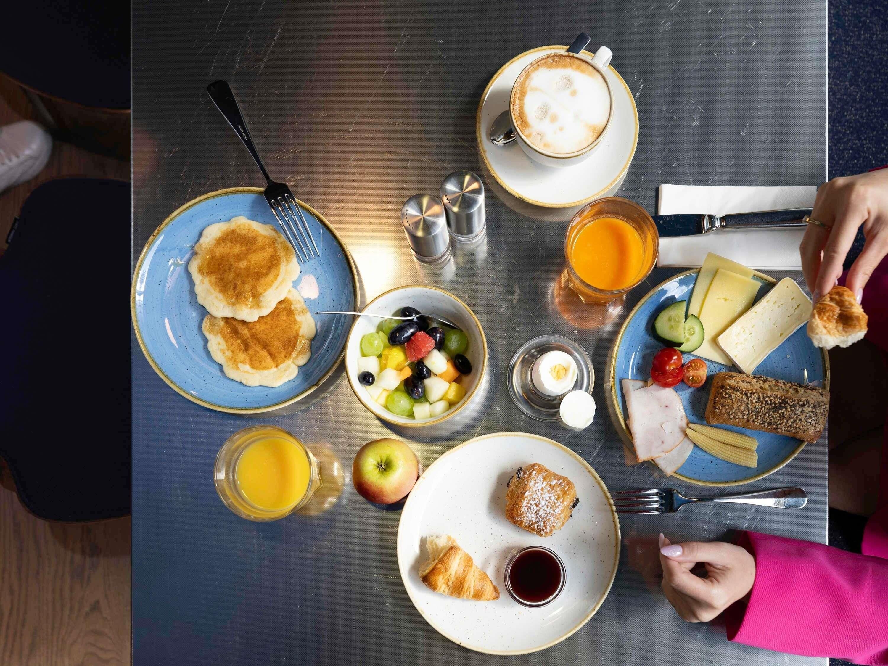 Une table dressée pour le petit-déjeuner, avec des crêpes, des fruits, du jus et un croissant.