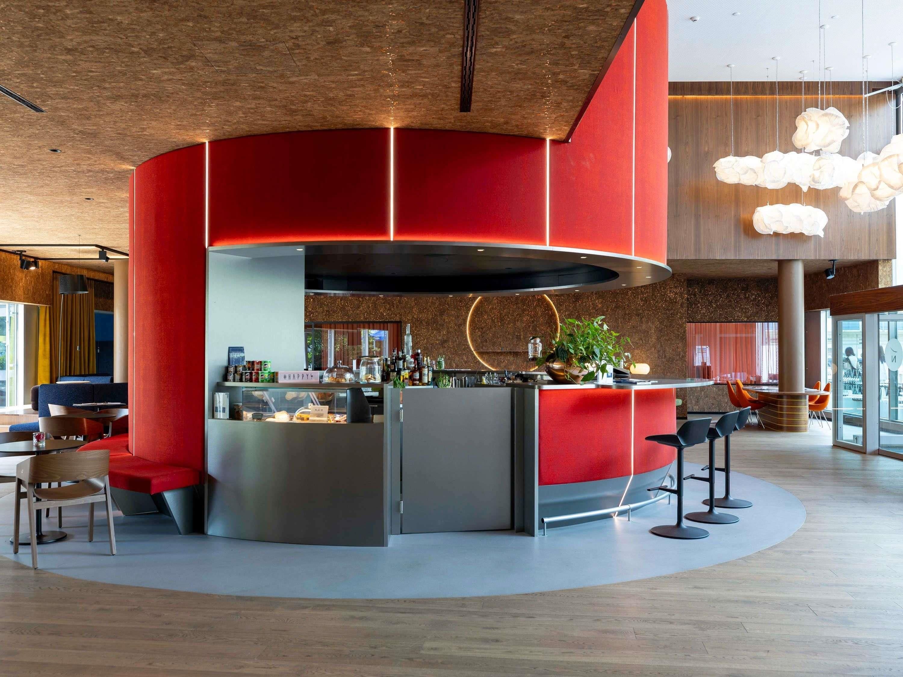 A modern bar area with a curved counter, seating, and a large overhead light fixture.
