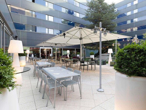 An outdoor patio area with tables and chairs, umbrellas, and potted plants.