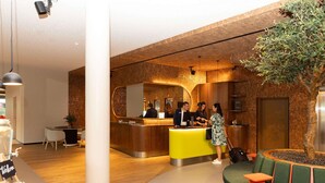 Een moderne hotel lobby met een receptiebalie, een zithoek en een grote boom.