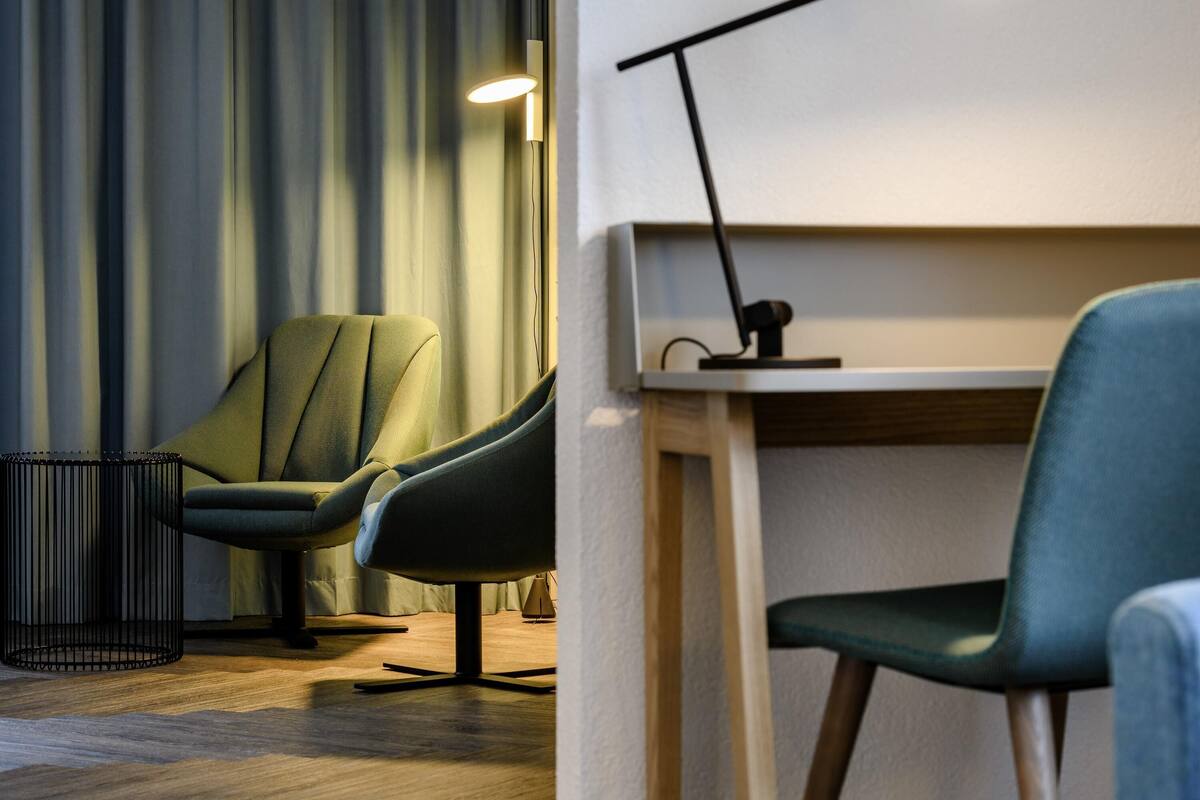 Une chambre moderne avec un fauteuil vert, un bureau en bois et un lampadaire noir.