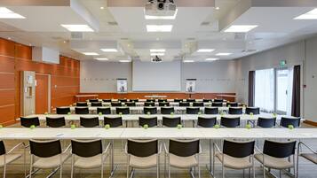 Une salle de conférence équipée de plusieurs tables et chaises, d’un projecteur et d’un grand écran.