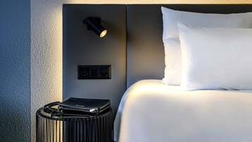 Una cama bien hecha con sábanas blancas, una mesita de noche negra con lámpara y un bolso pequeño negro al lado.