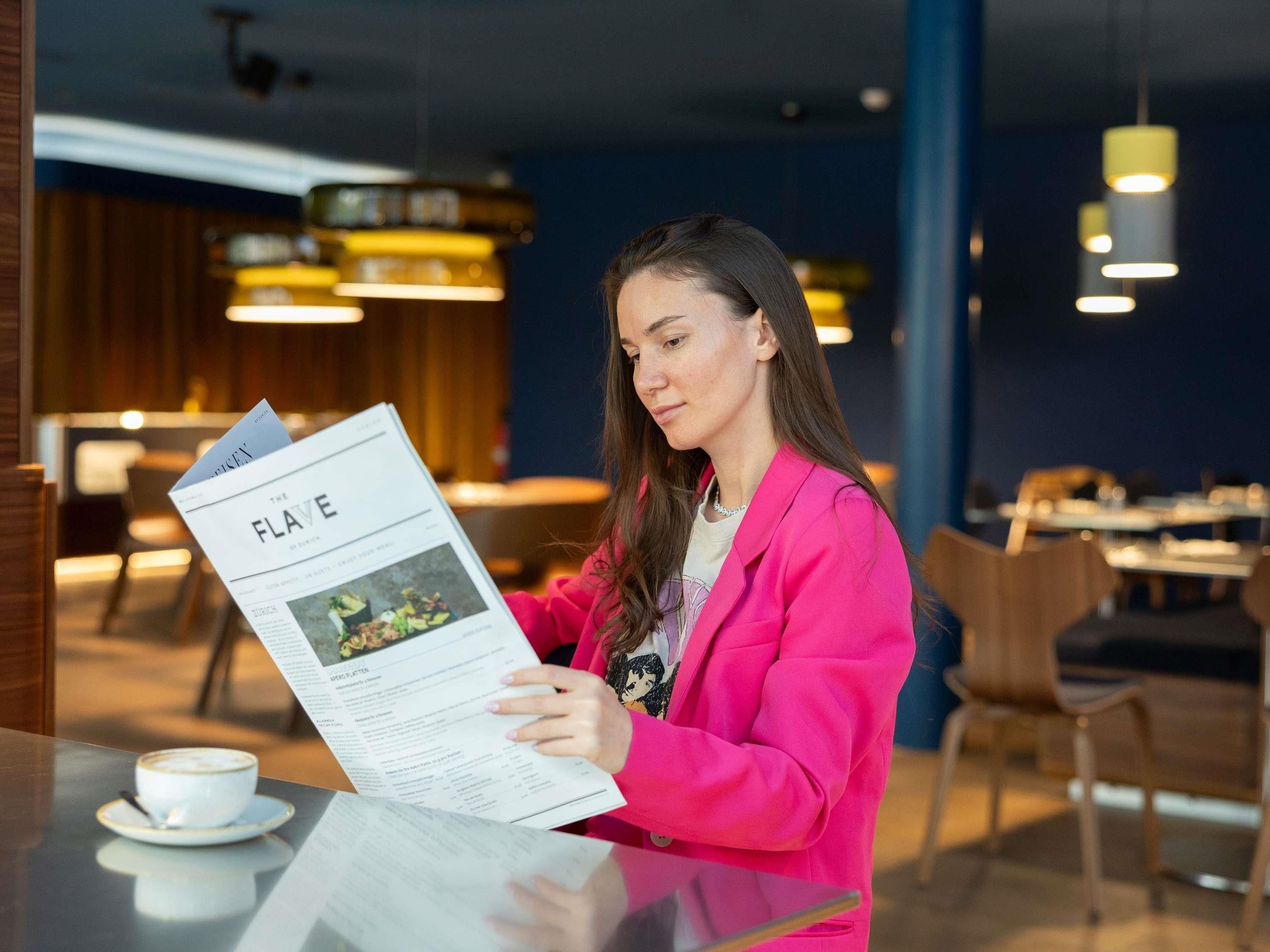 A person reading a menu at a table in a modern indoor setting with seating and pendant lighting.