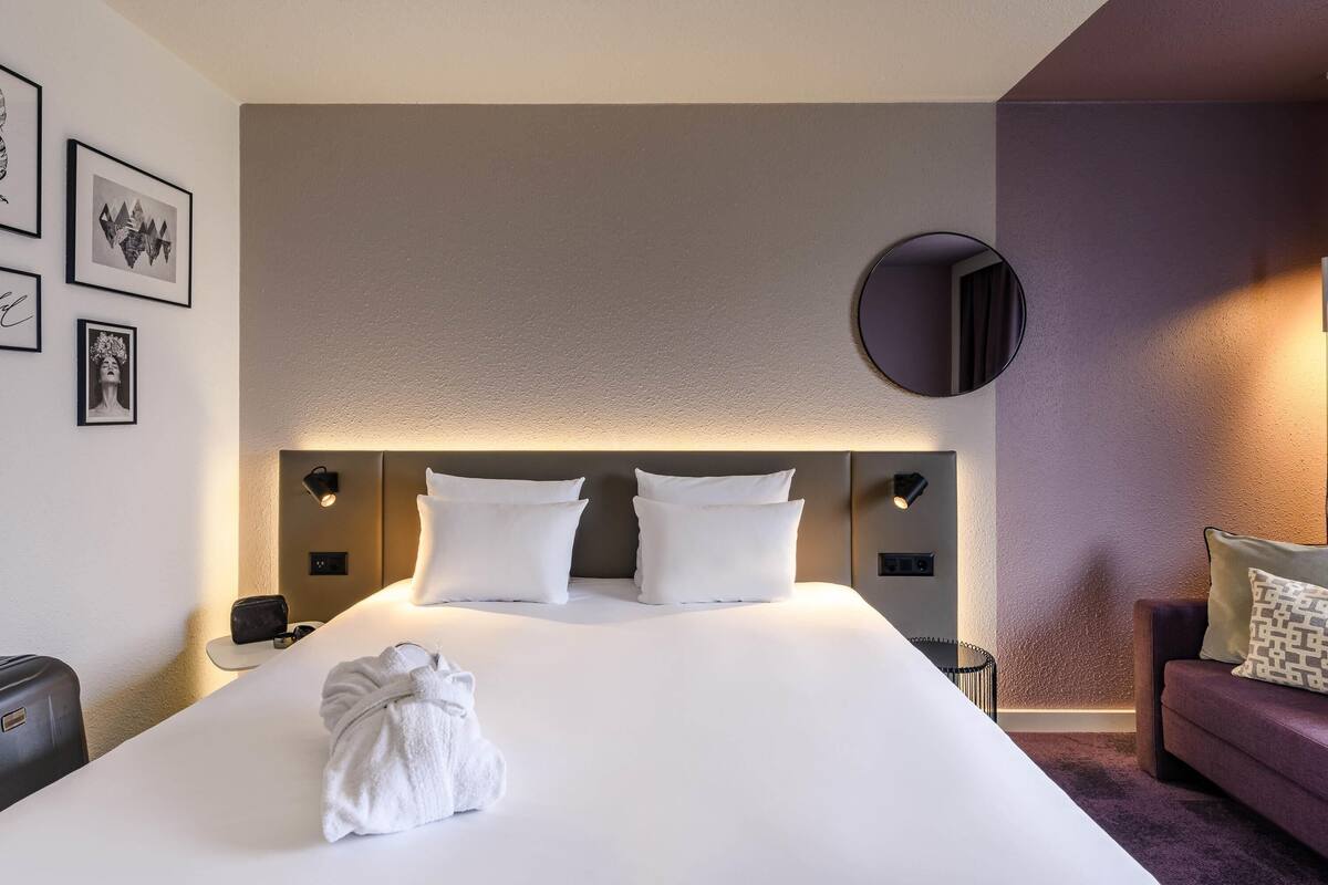 Hotellihuone, jossa on suuri sänky, pyöreä peili ja pieni pöytä, jossa on lamppu.