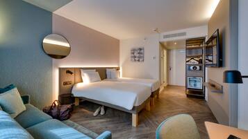 A modern hotel room with a large bed, a sofa, a desk, and a wardrobe.