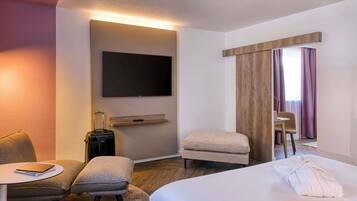 A hotel room with a bed, a desk with a chair, a small table, a television, and a window with curtains.