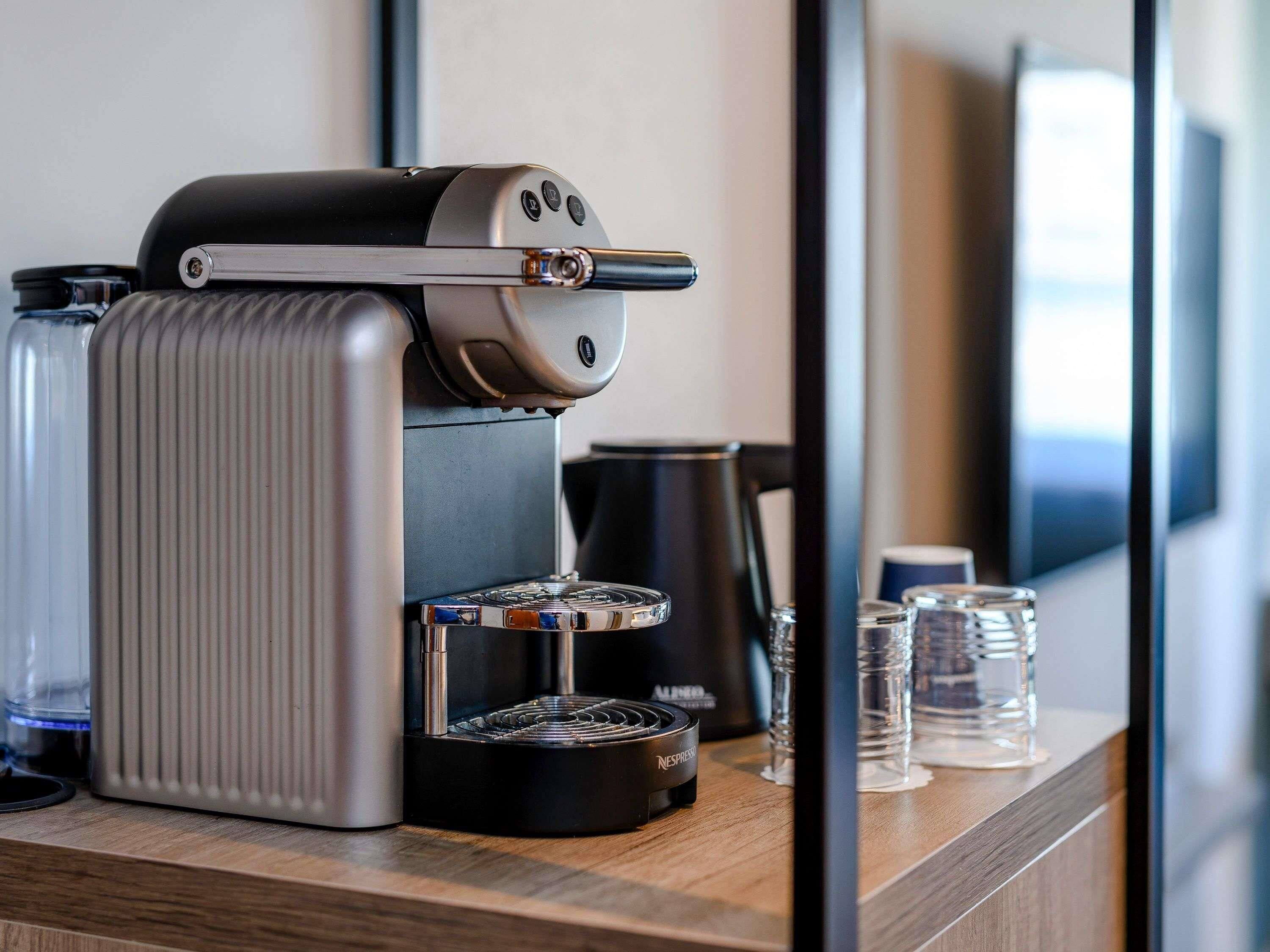 A Nespresso coffee machine on a wooden counter with a black coffee pot and clear glasses.