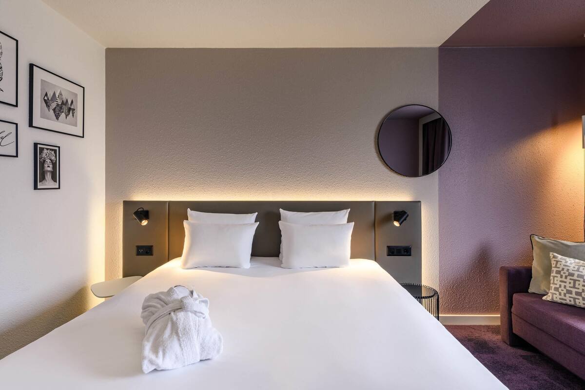 Quarto de hotel com uma cama grande, um espelho redondo e um sofá.