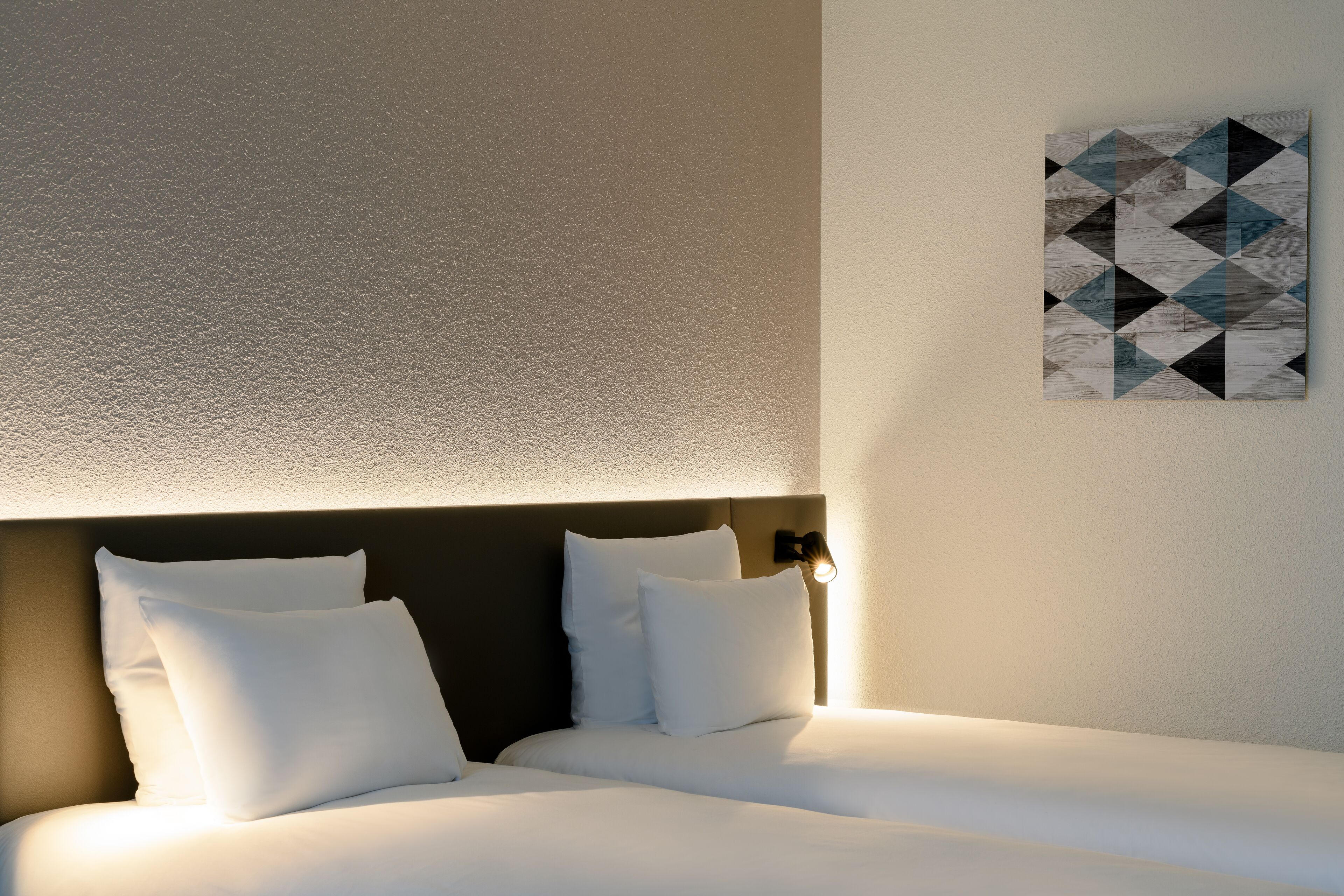 Una camera d'albergo con un letto rifatto, una testiera con un lampadario e un quadro a parete con motivi geometrici.