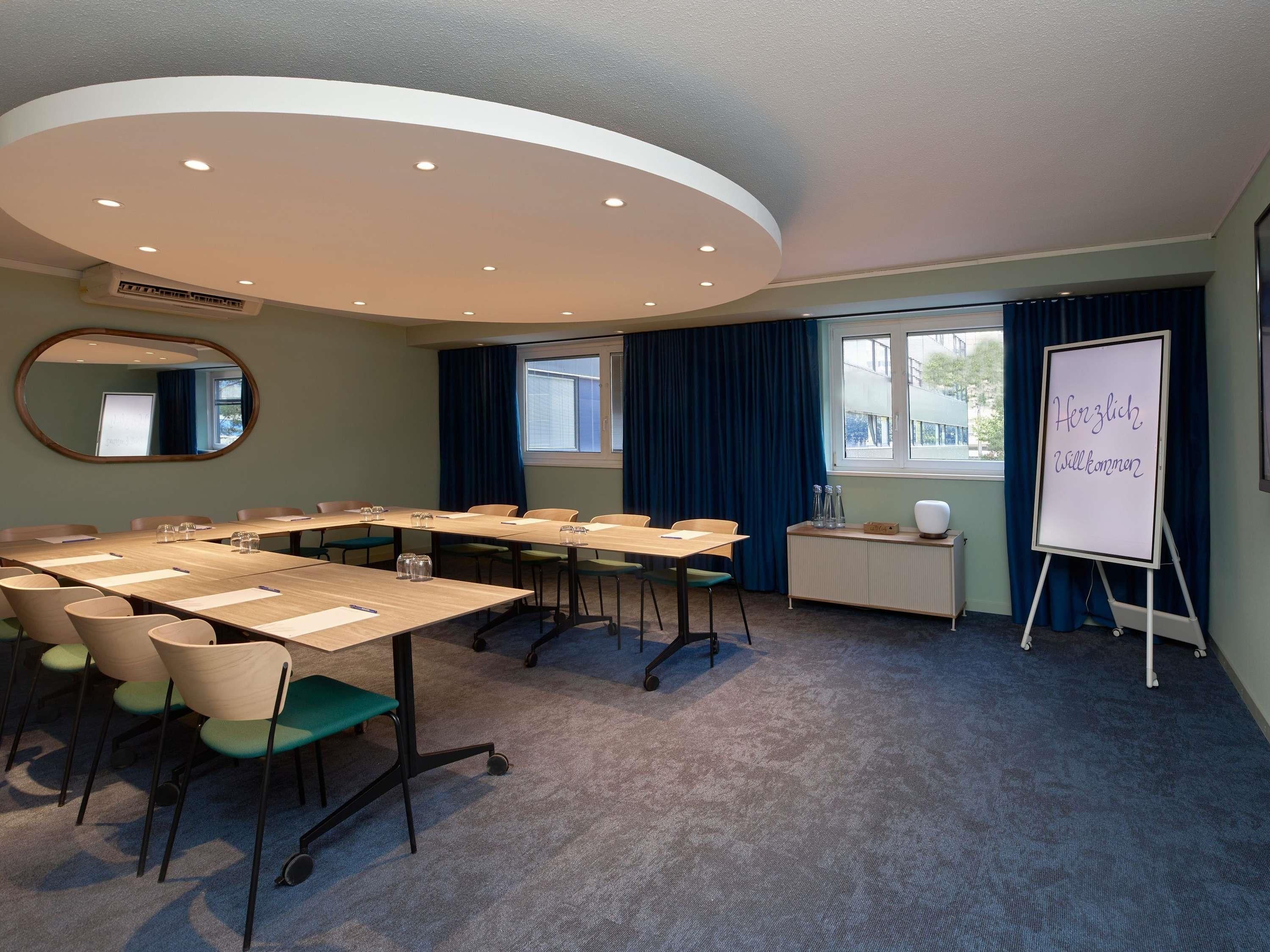 A conference room with a long table, chairs, a whiteboard, and a window with curtains.