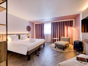 Hotellihuone, jossa on sänky, tuoli, työpöytä, matkalaukku ja kannettava tietokone.