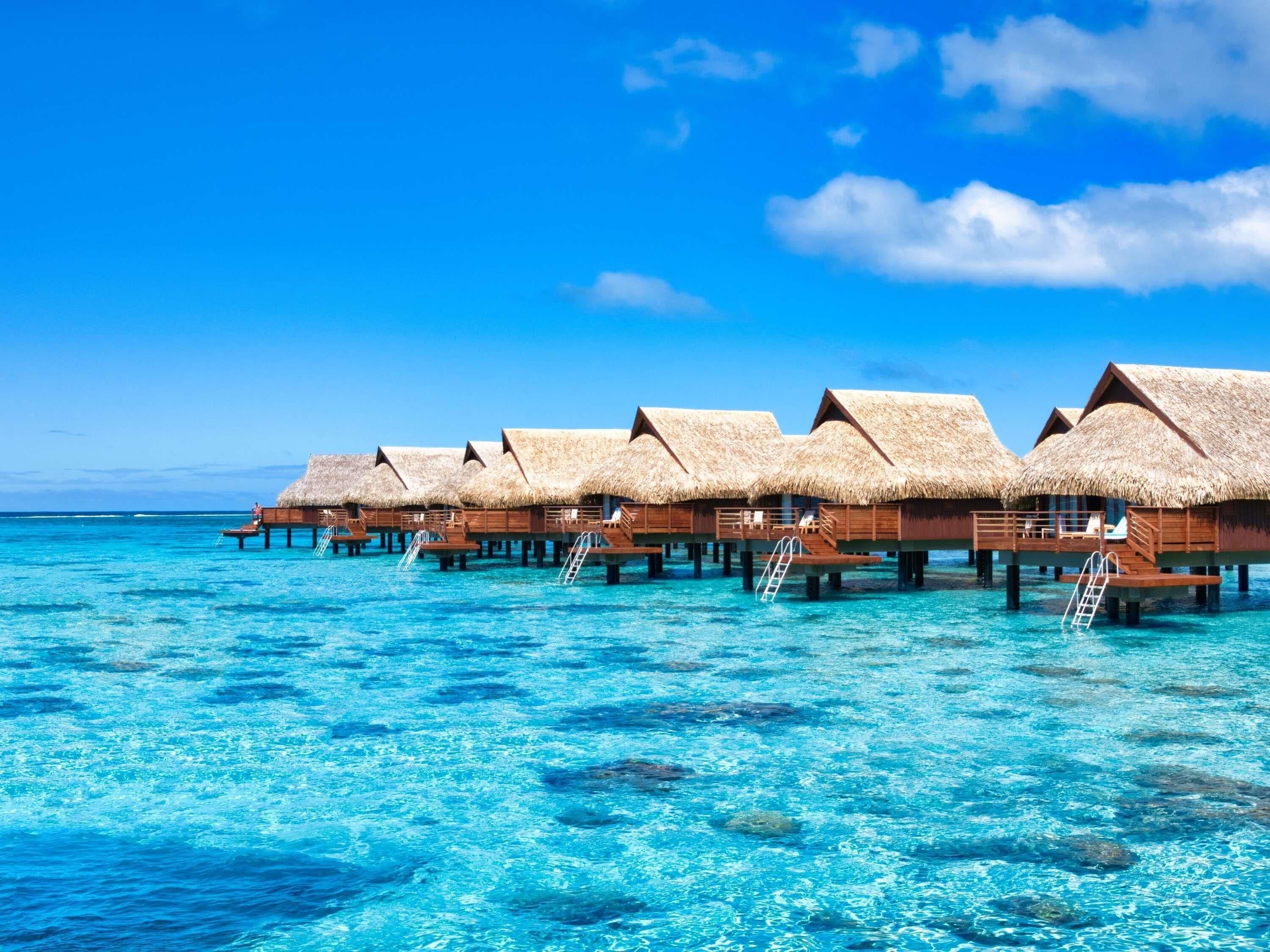 Overwater bungalows with thatched roofs, wooden walkways, and clear blue water.