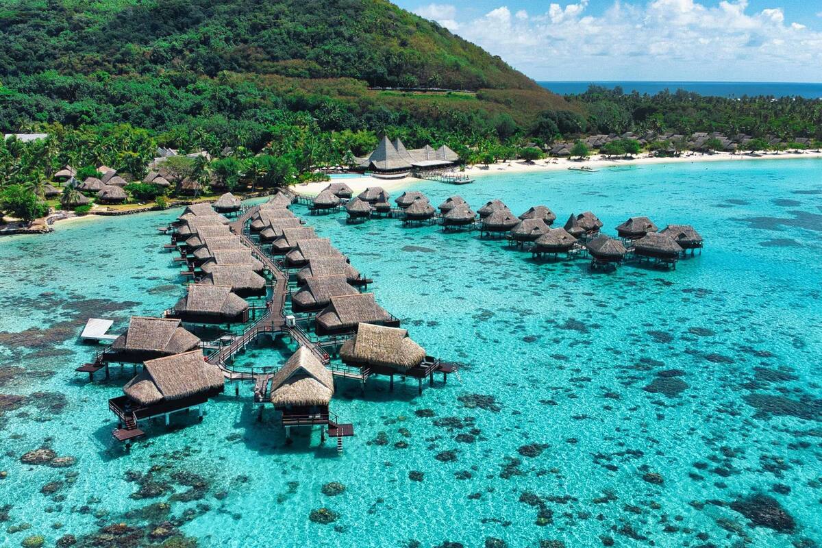Zona de bungalows sobre el agua con techos de paja, agua turquesa cristalina y un exuberante telón de fondo verde.