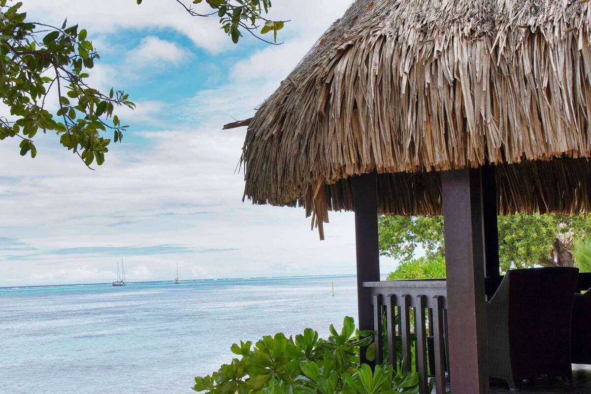 Una edificación con techo de paja y vista al mar y veleros.