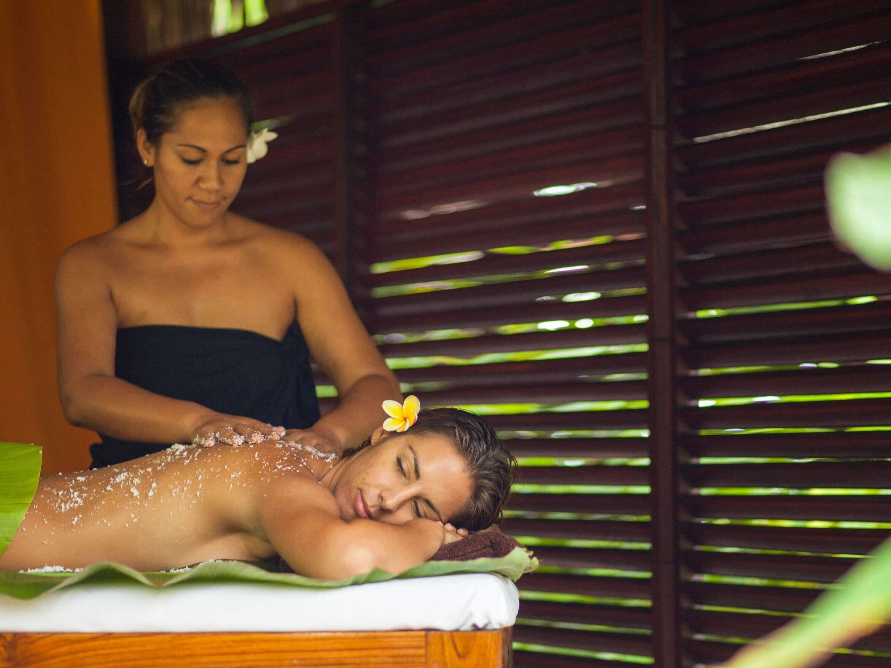 A person receiving a massage in a room with a wooden slatted wall and a green mat on the floor.