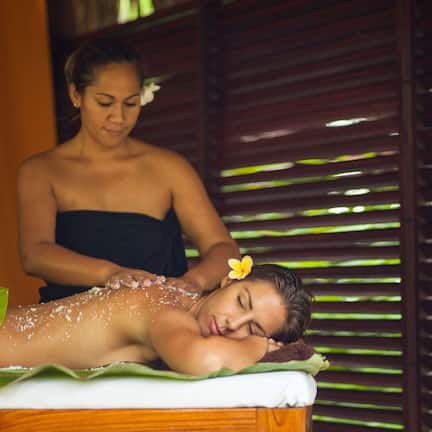 A person receiving a massage in a room with a wooden slatted wall and a green mat on the floor.