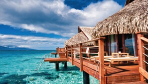 Een houten overwaterbungalow met rieten dak, een houten terras en een helder uitzicht op de turquoise zee.