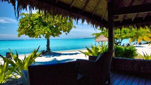 Un salón junto a la playa con vista al océano, techo de paja y sillones de descanso.