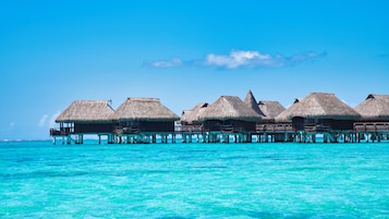 Overwater bungalows with thatched roofs on stilts, connected by walkways, over turquoise ocean water.