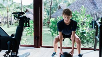 A person performing a squat exercise with a medicine ball in a room with a treadmill and large windows overlooking a garden.