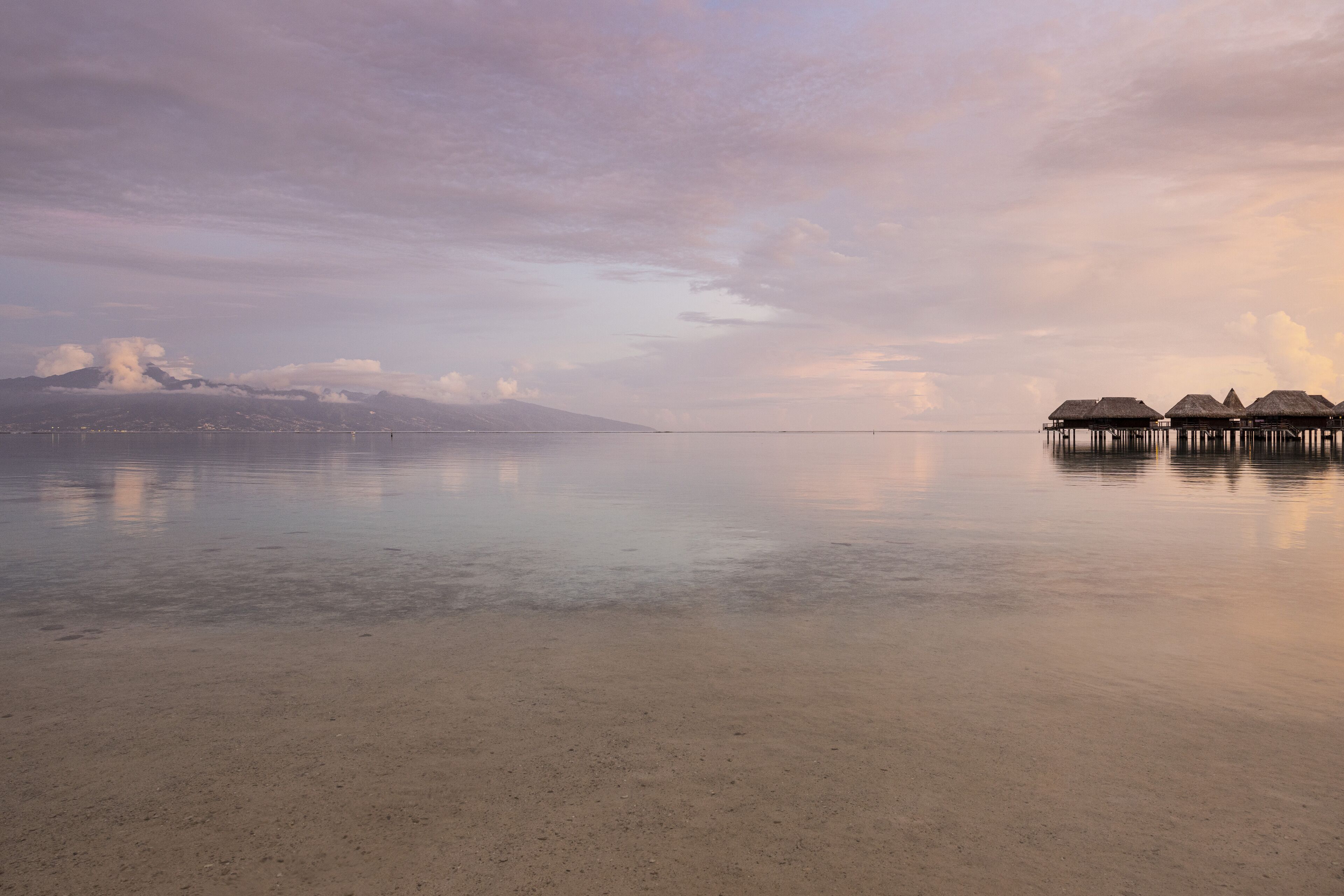 A beach with overwater bungalows and a mountain in the background.