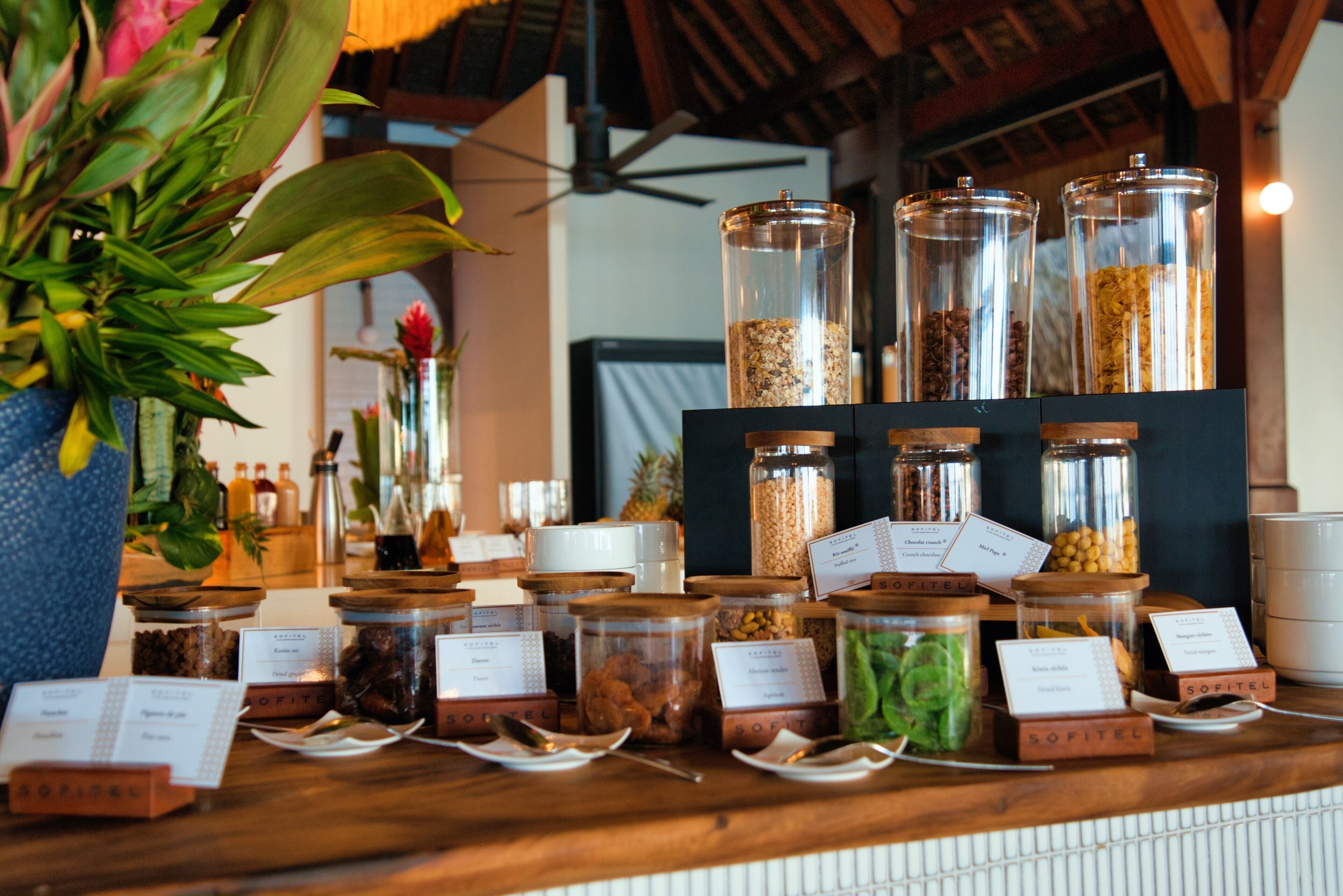 A display of various food items in glass jars with labels, arranged on a wooden counter.