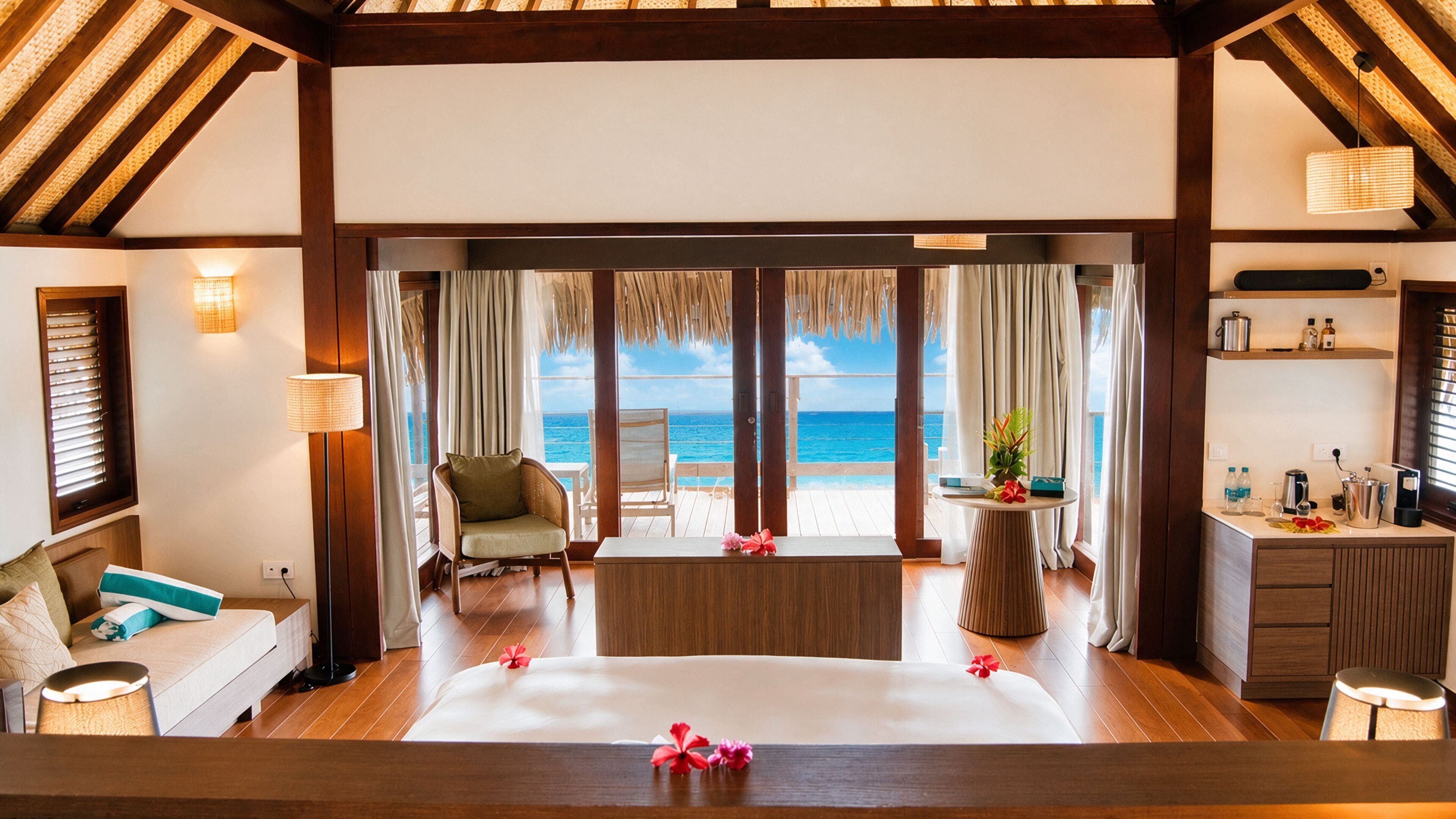 A room with a bed, a chair, a table, and a view of the ocean.