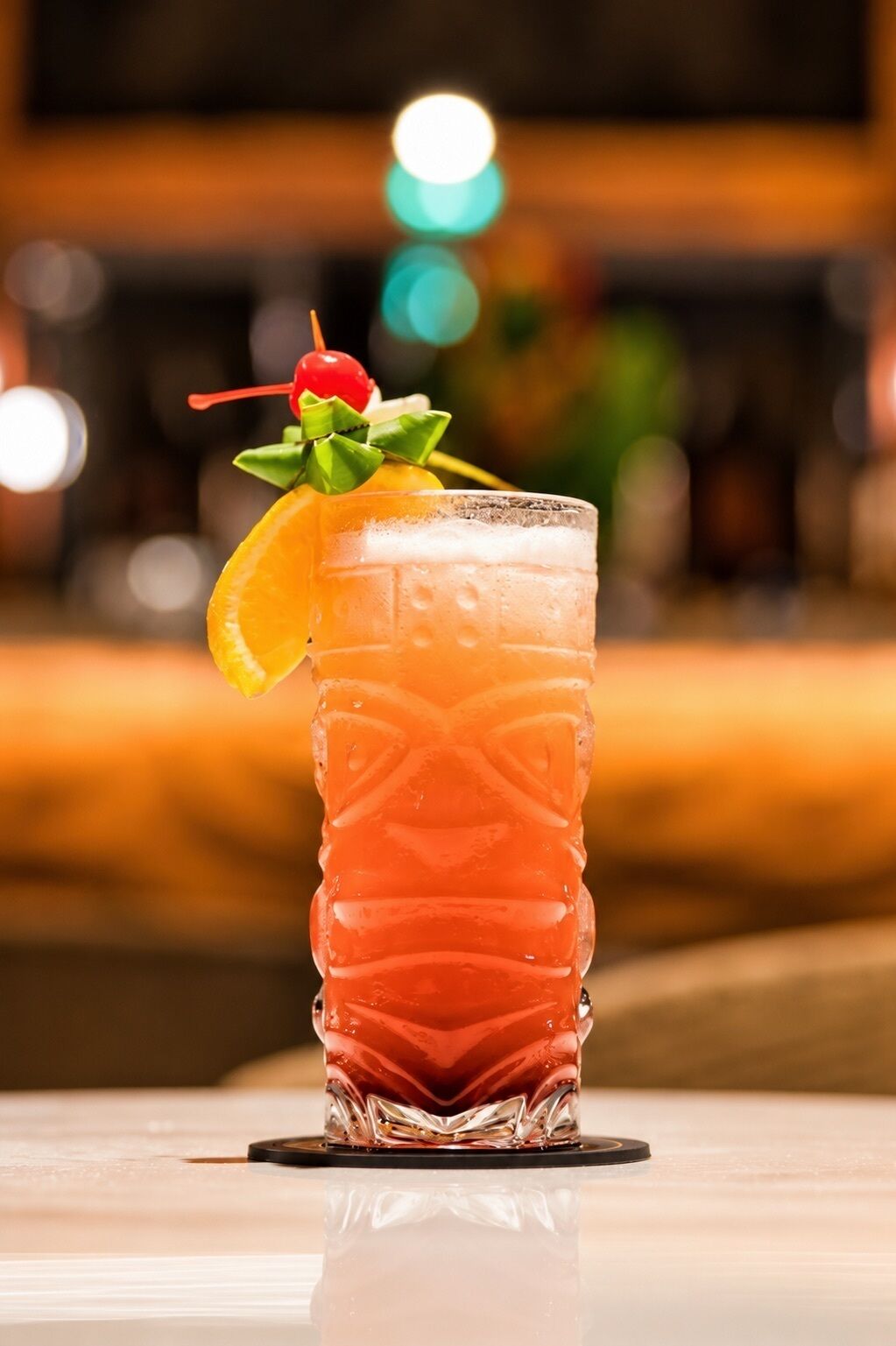 A tall glass with a textured pattern, containing a beverage garnished with a cherry, orange slice, and green leaves.