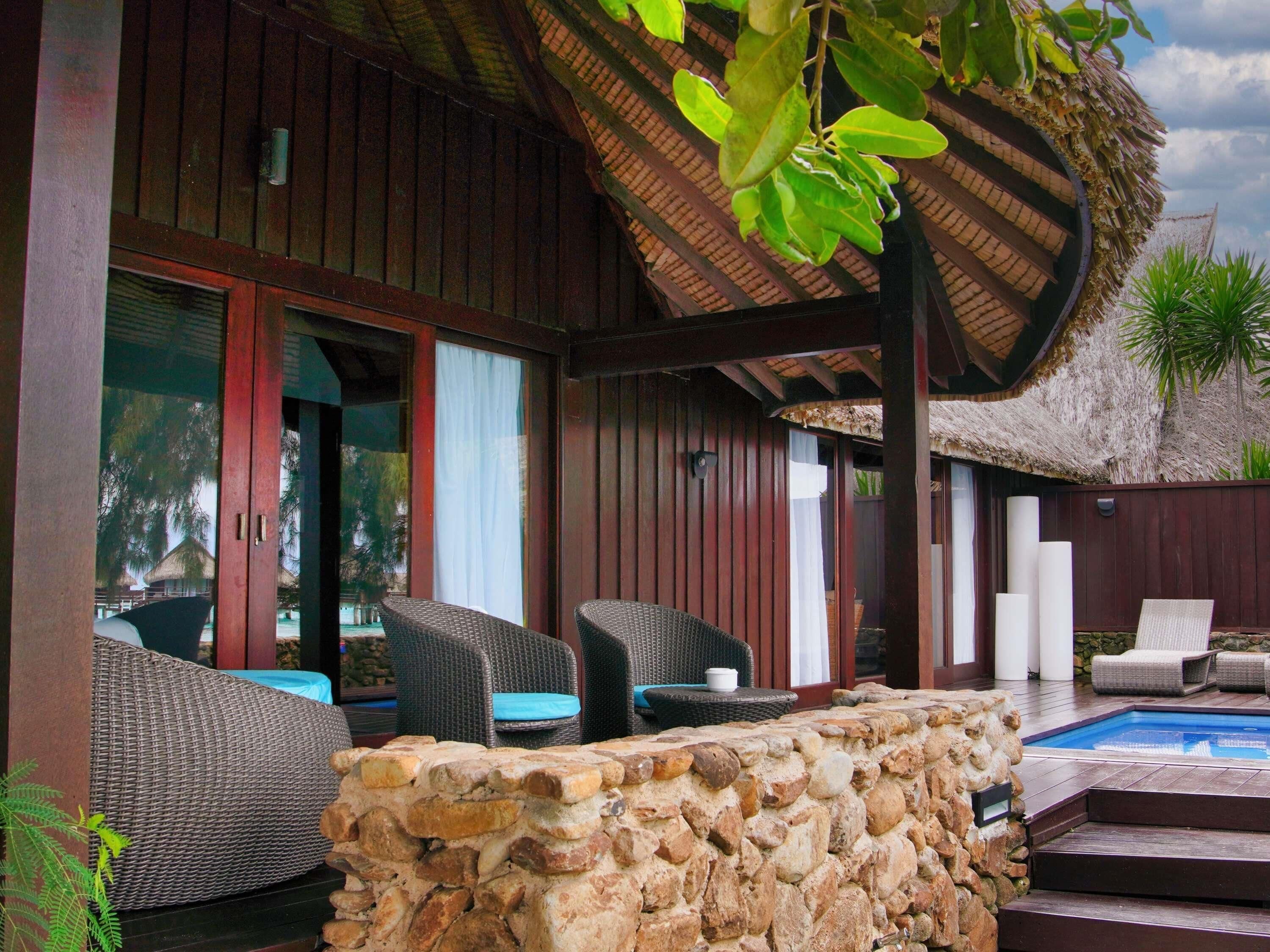 A covered outdoor area with wicker furniture, a stone wall, and a pool.