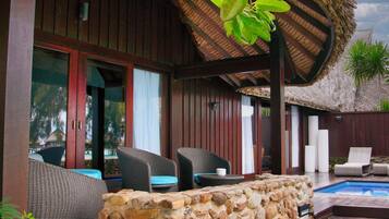 A covered outdoor area with wicker furniture, a stone wall, and a pool.