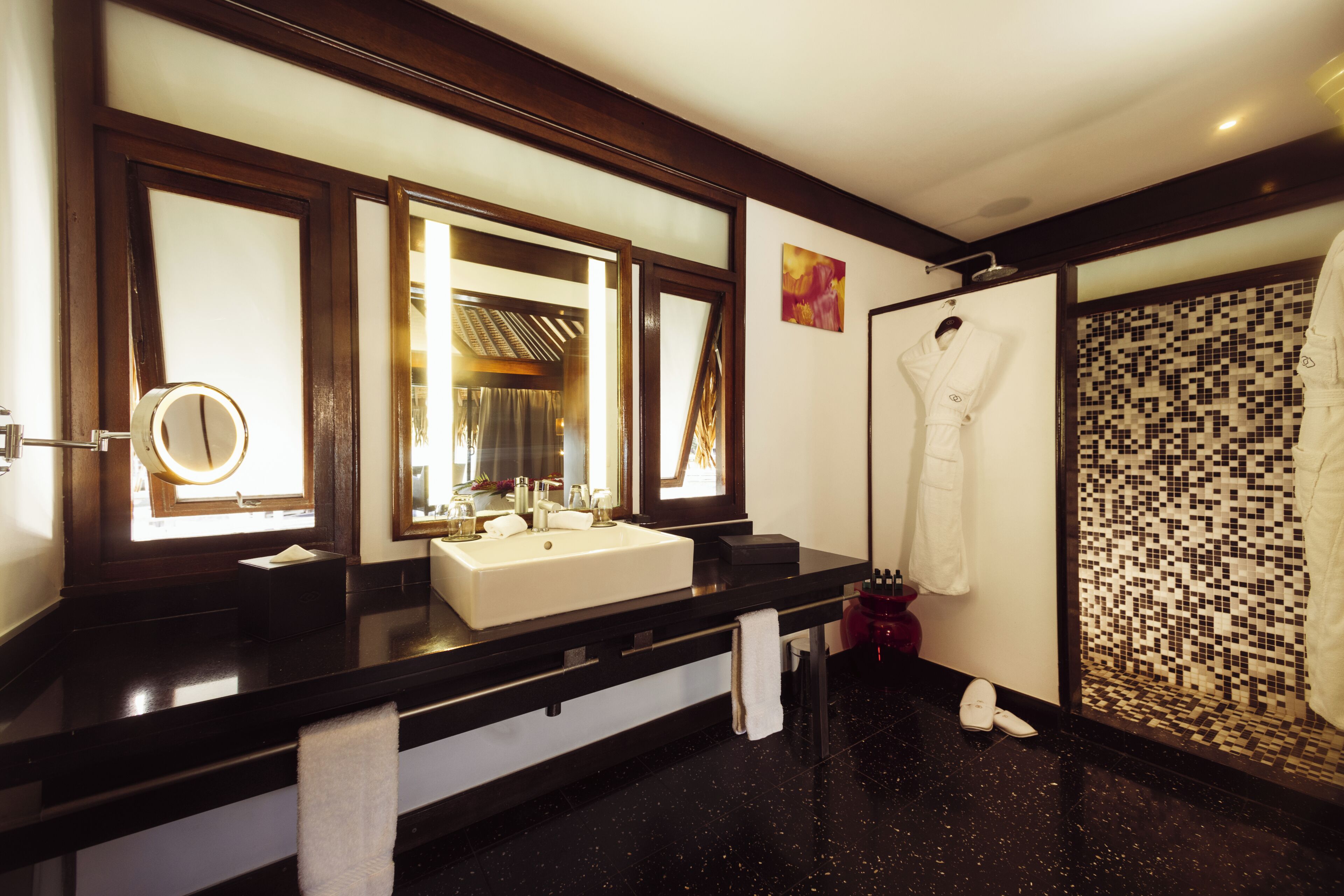 A hotel bathroom with a black countertop, a white sink, a mirror, and a shower area.