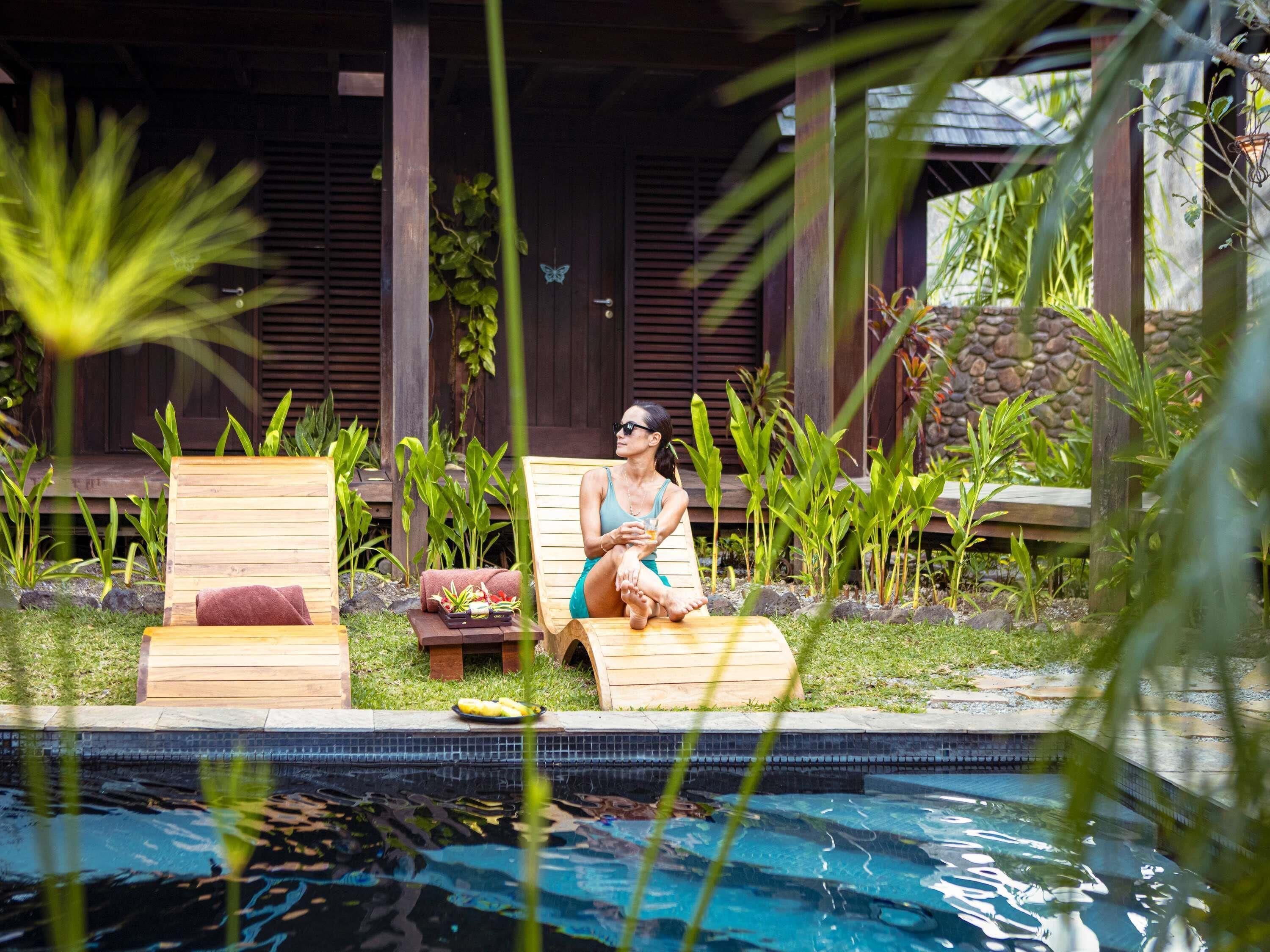 A poolside area with wooden loungers, a small table with fruits, and a stone wall in the background.